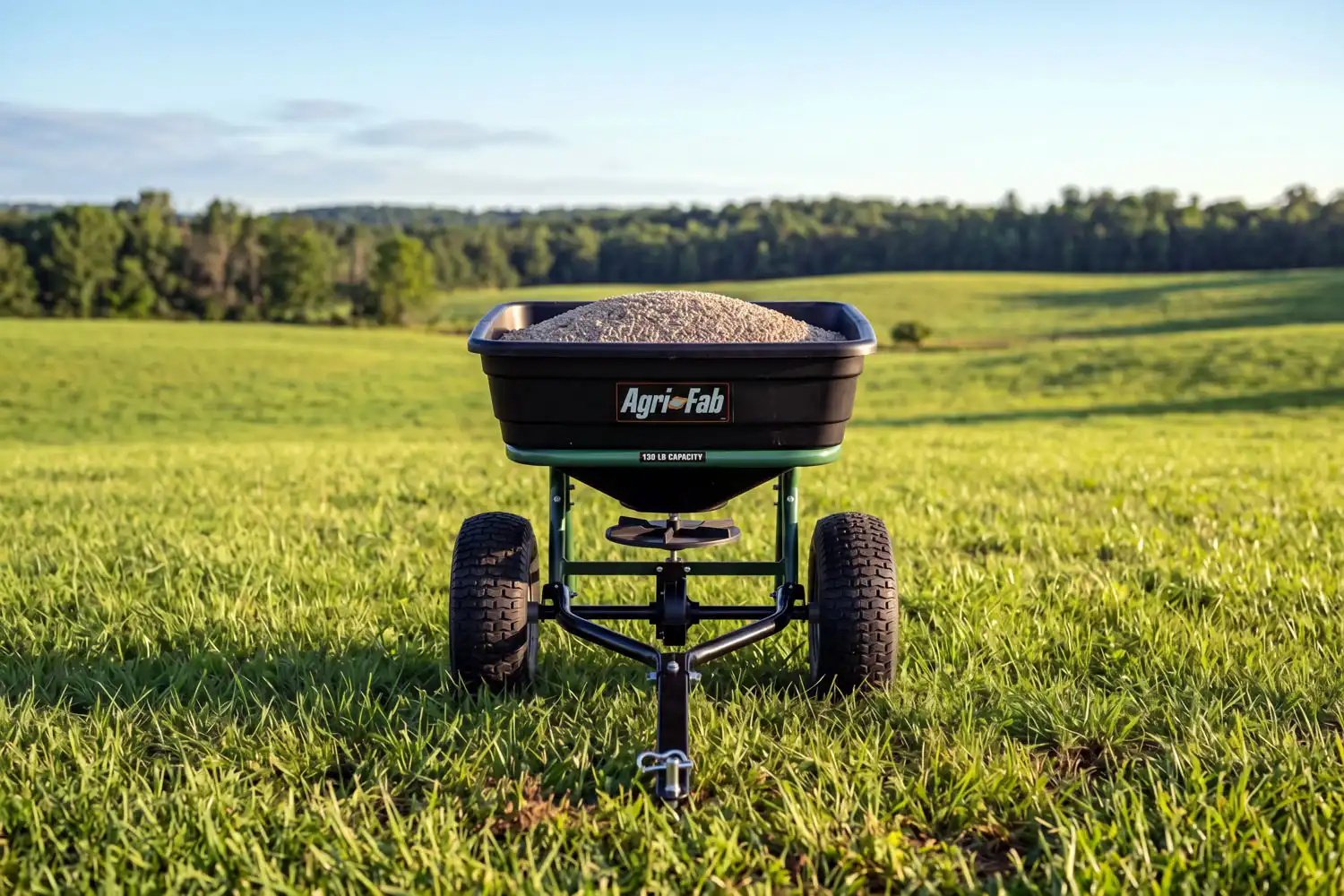 Brand new tow behind broadcast spreader with full hopper standing on a green farm field