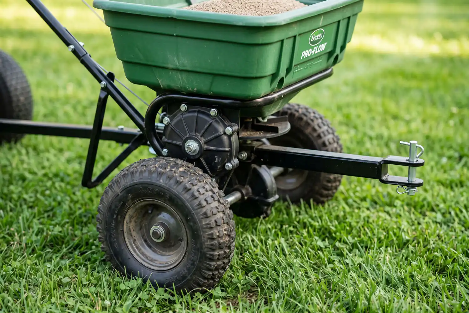 A tow behind broadcast spreader showing hopper, gearbox, hitch, and pneumatic tire